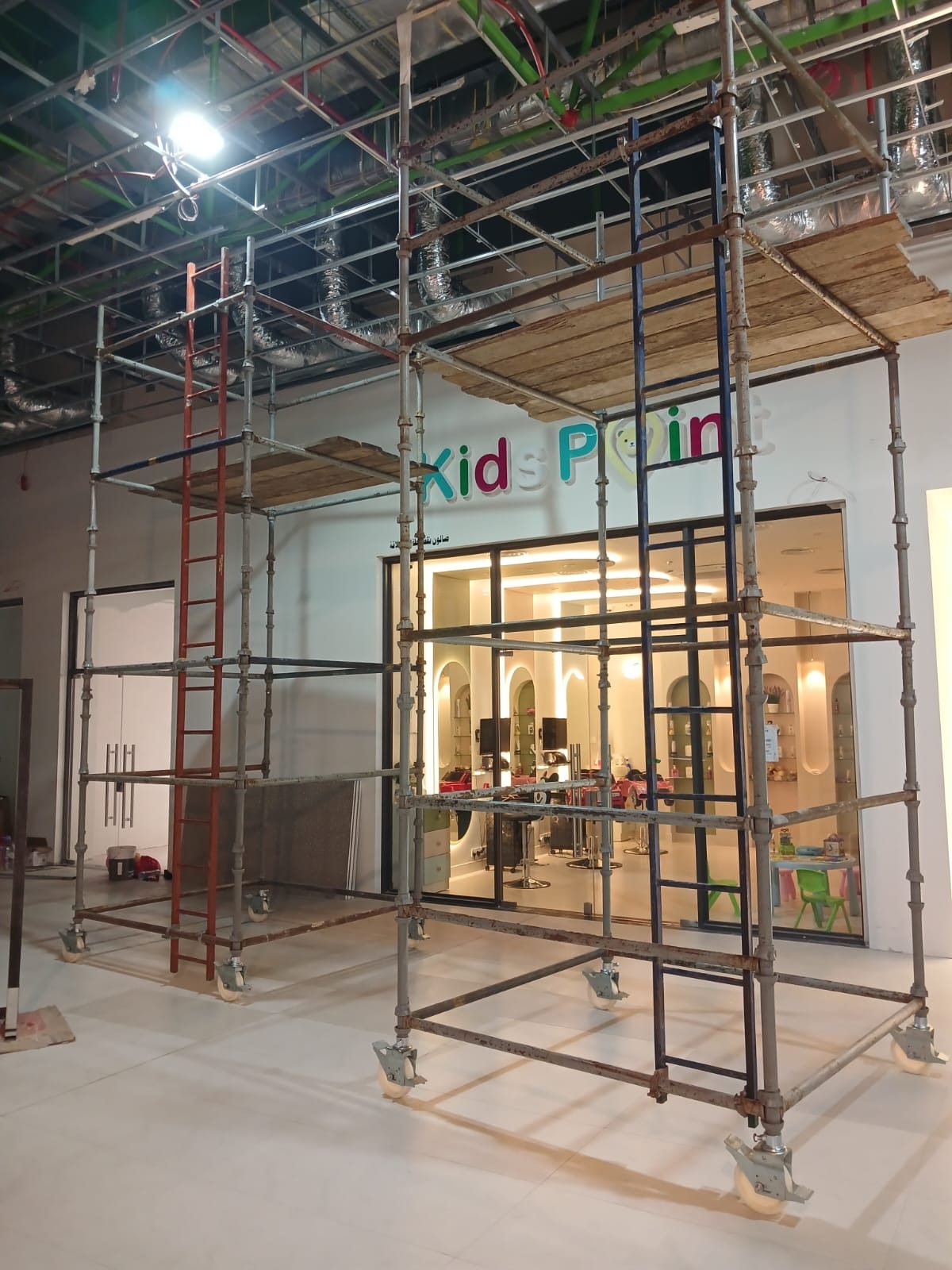 Mobile scaffold tower with safety-vested crew working around it inside a shopping mall under fit-out