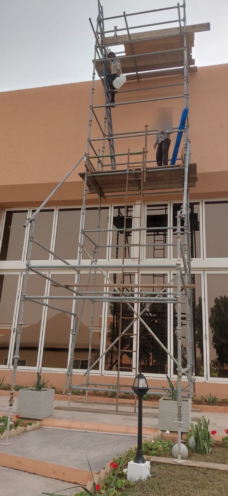Two workers on boarded platforms of a high scaffold tower at a residential villa site