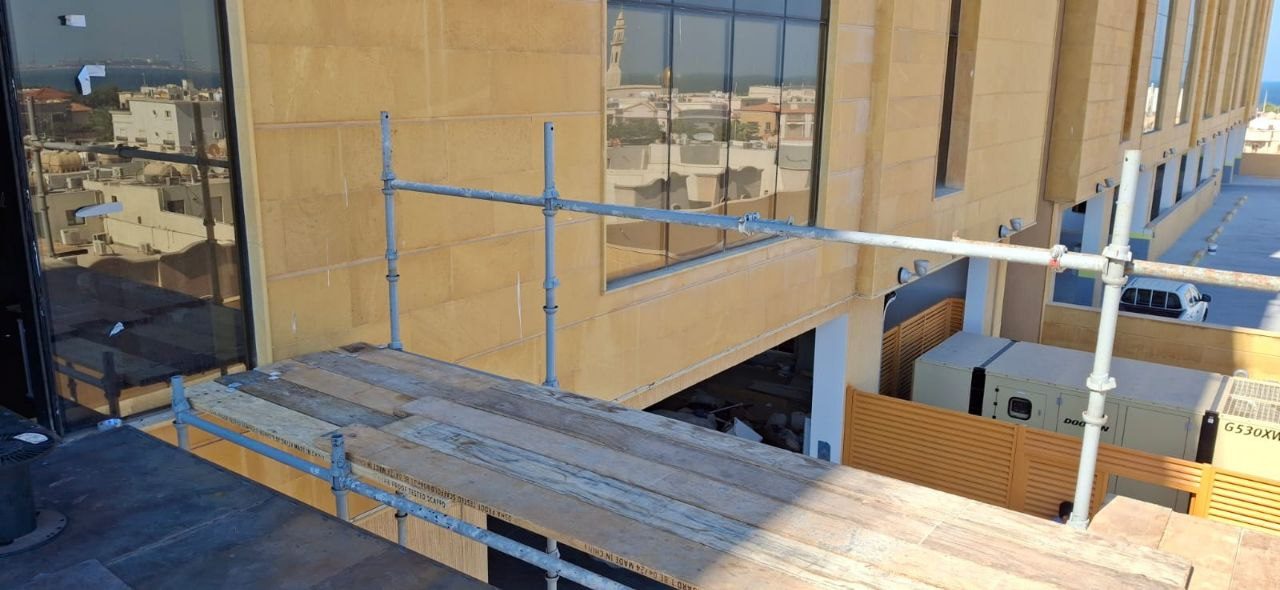 Elevated scaffolding platform with timber decking at a multi-storey commercial building exterior overlooking the city