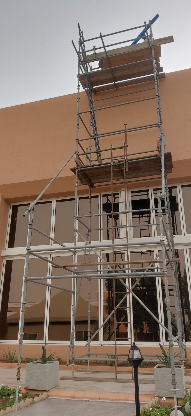Multi-level scaffold tower with boarded platforms against a villa glass facade