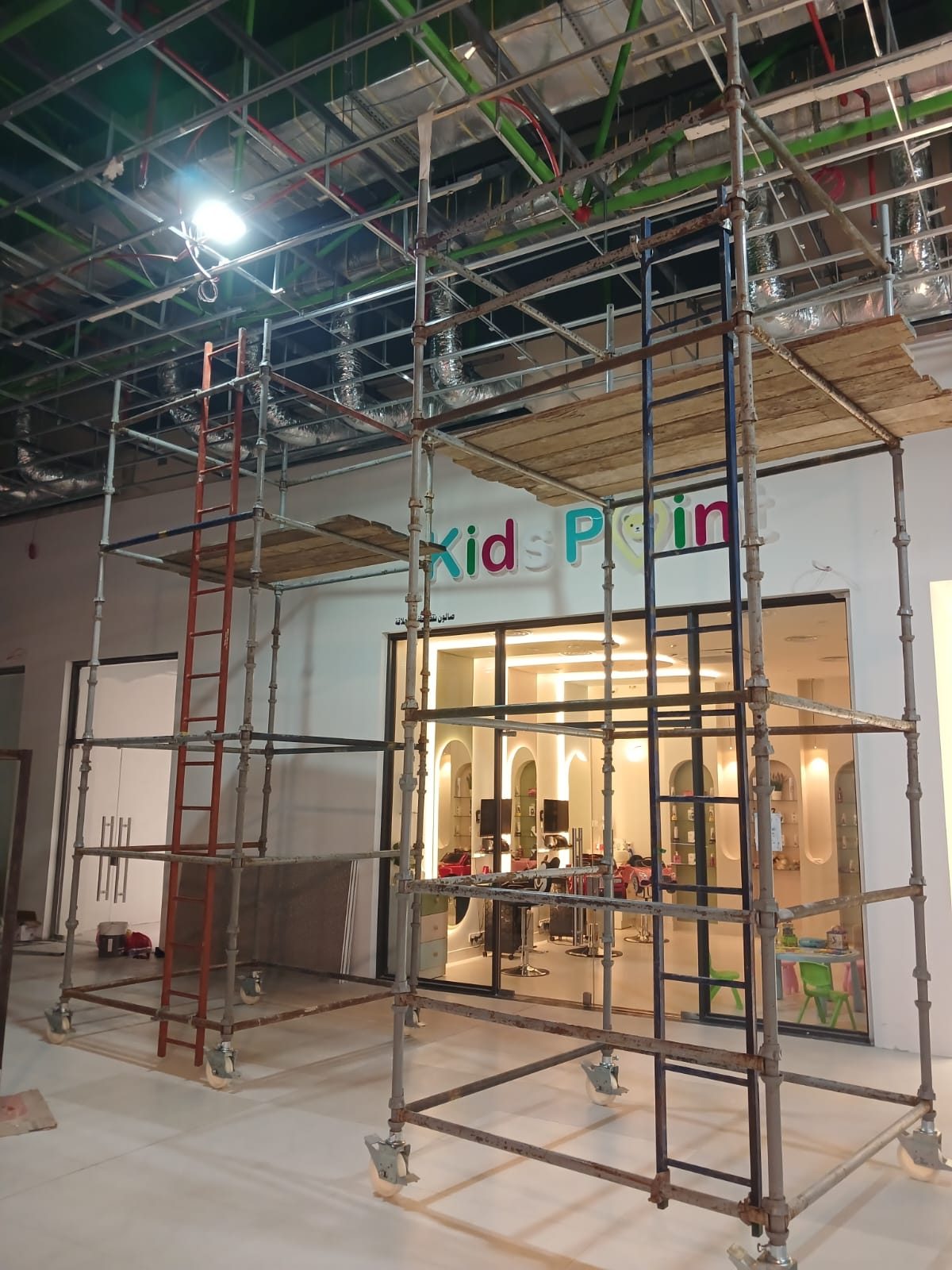 Freestanding scaffold tower on castors with a boarded platform positioned in a busy shopping mall concourse