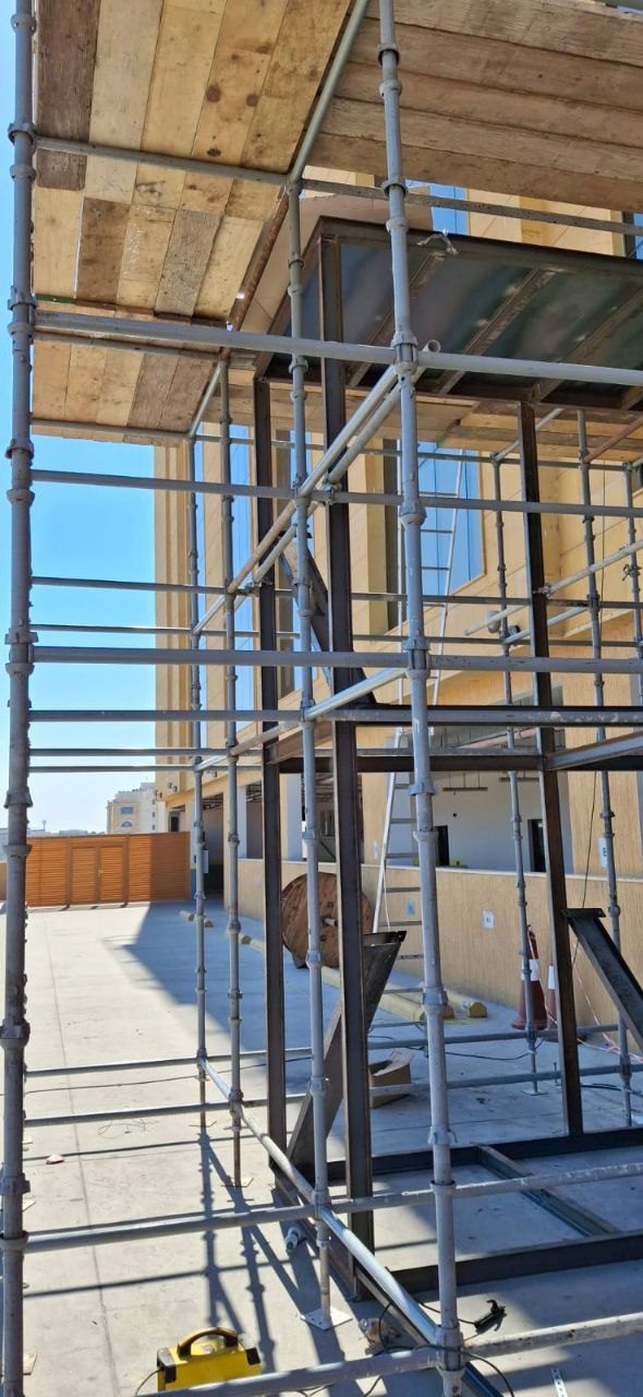 Tube-and-clamp scaffolding with timber platforms providing access to a stone and glass commercial building facade