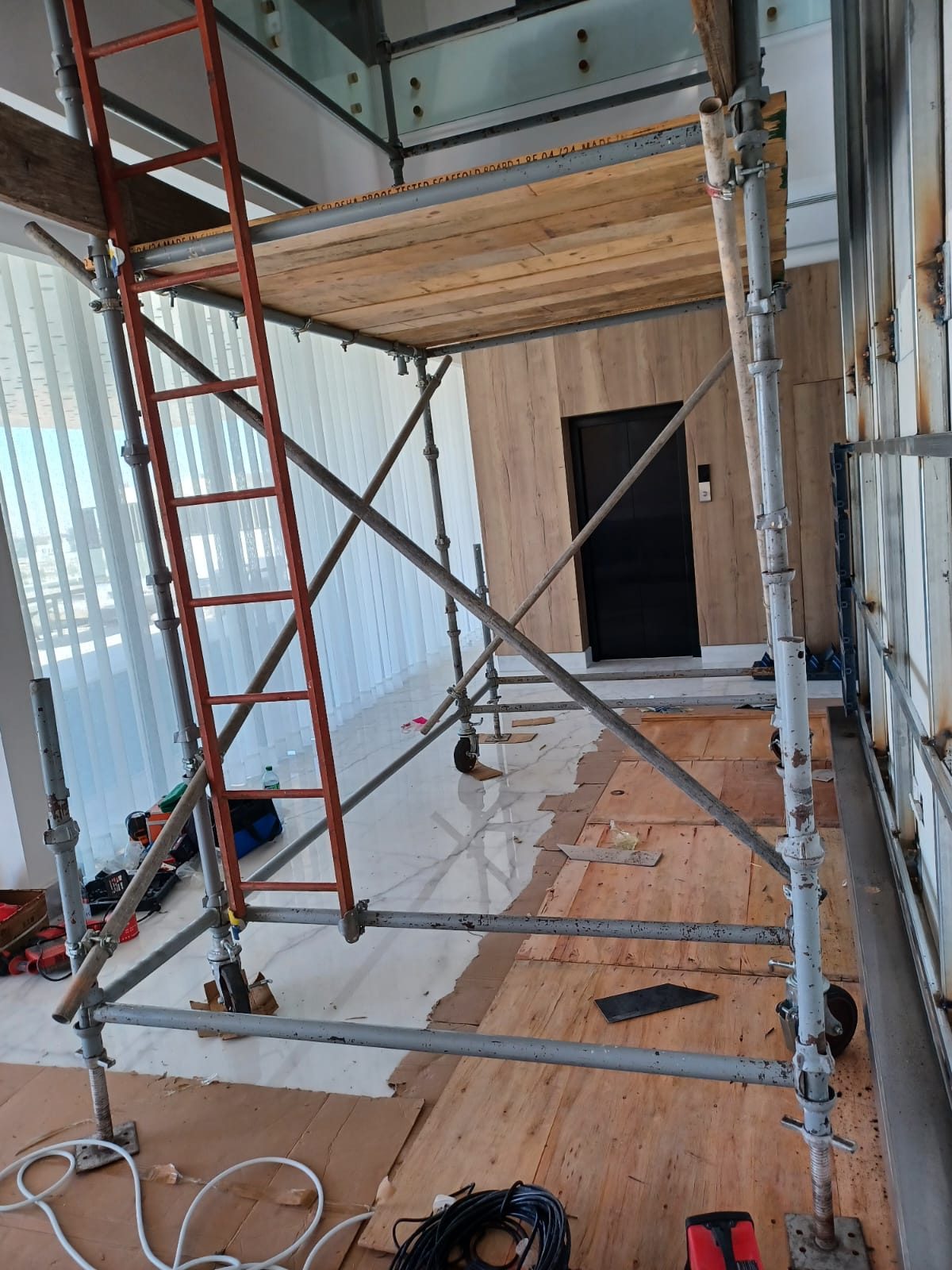 Upward view of boarded scaffold platforms and ladder access within a tall glazed interior space