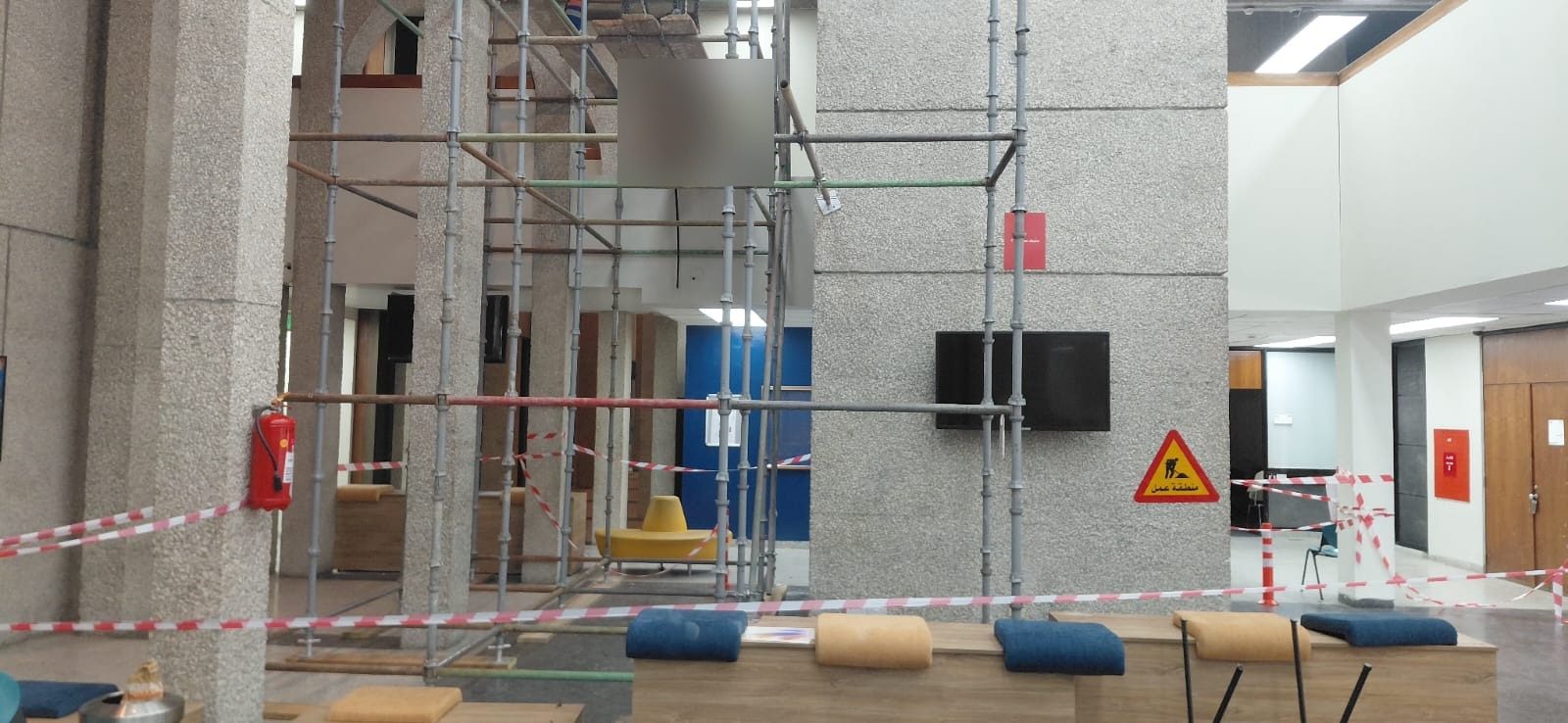 Wide view of an interior atrium with multi-level scaffolding, seating areas and safety warning tape