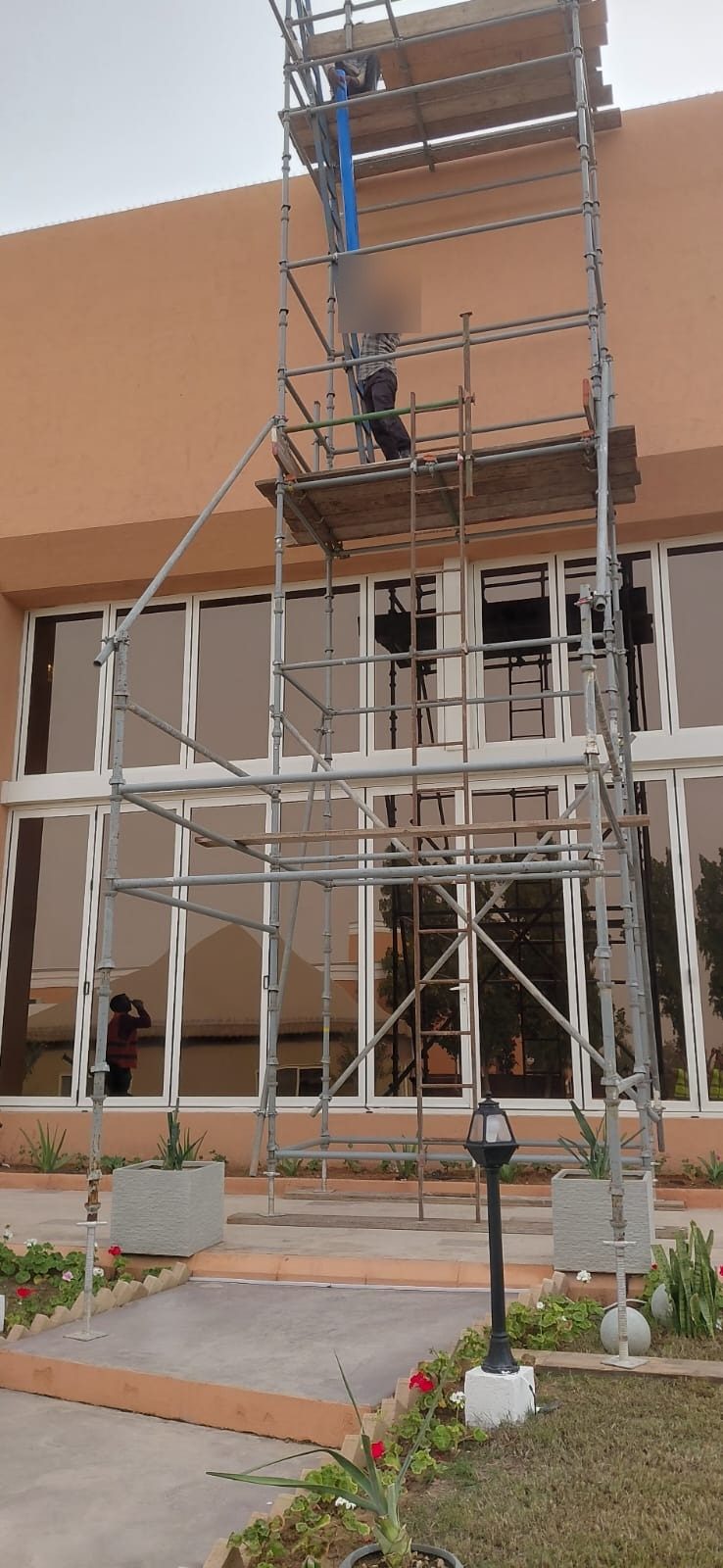 Worker climbing a tall scaffold tower during maintenance works on a residential villa facade