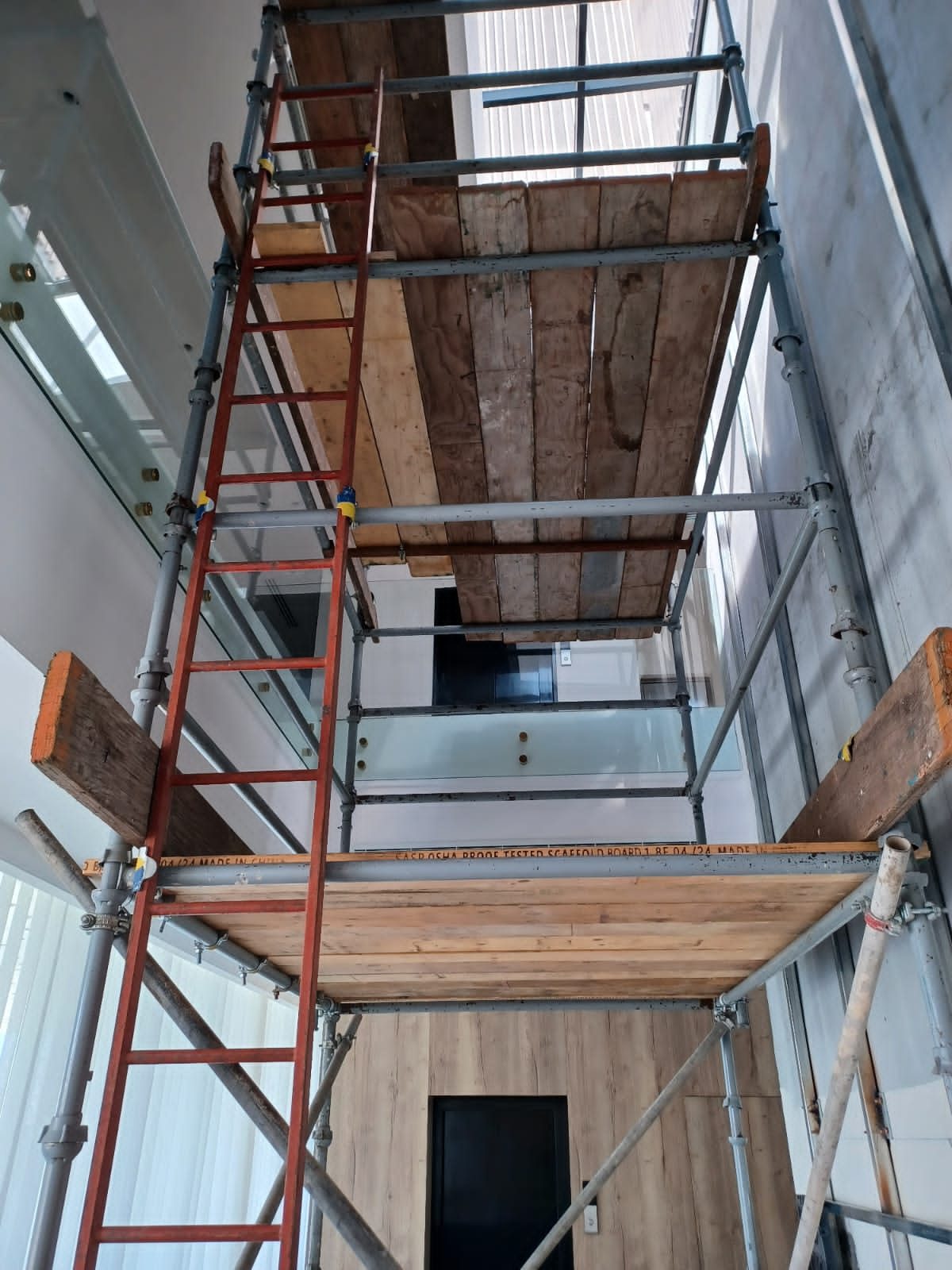 Multi-level tube-and-clamp scaffold with boarded platforms and ladder access inside a double-height building interior