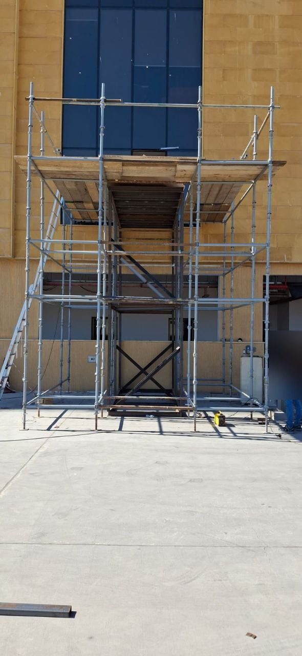 Full-height tube-and-clamp scaffolding tower erected against a multi-storey commercial building facade for glazing and facade works