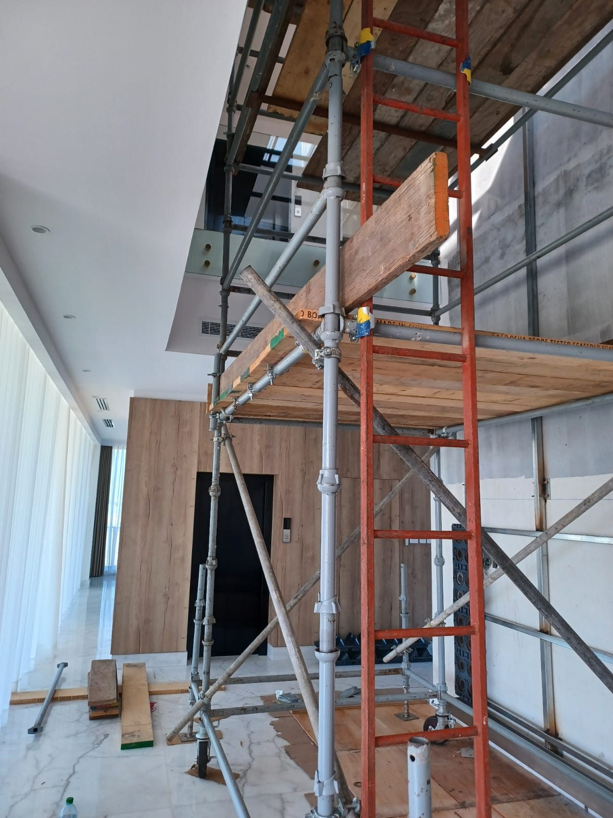 Side view of a braced mobile scaffold with ladder and timber platforms inside a finished building corridor