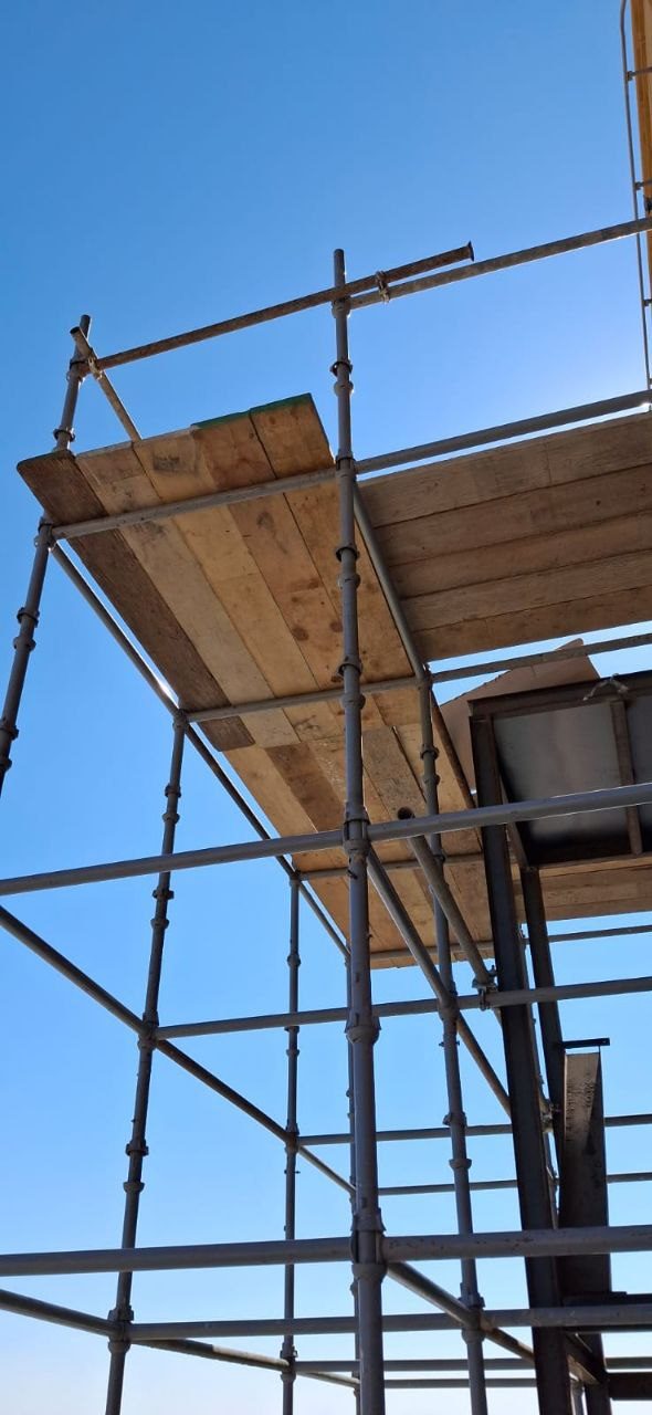 Close-up of tube-and-clamp scaffolding frames and timber platforms for commercial facade access