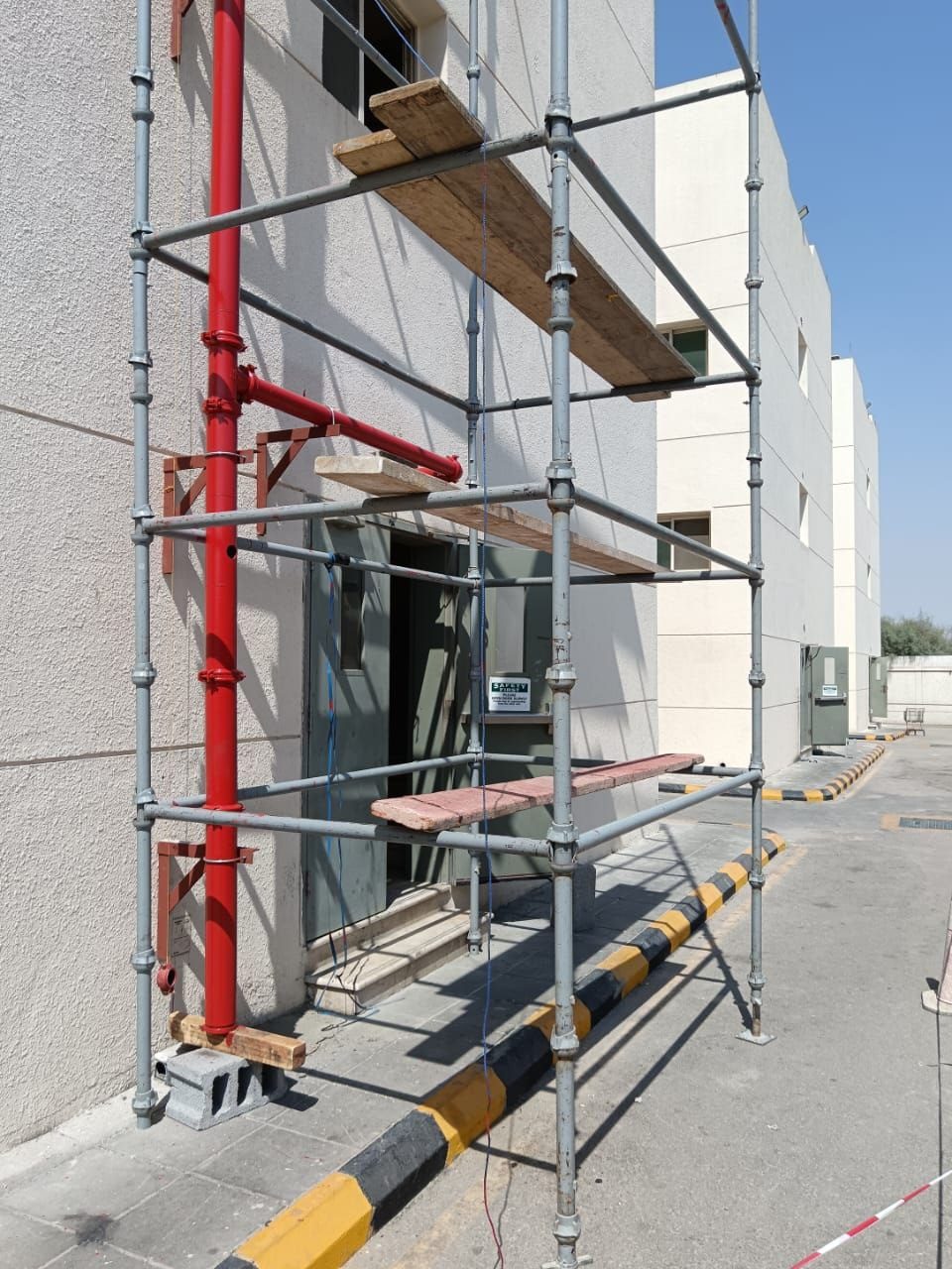 Close-up of scaffolding boards and frames providing access to a fire suppression pipe on a building exterior