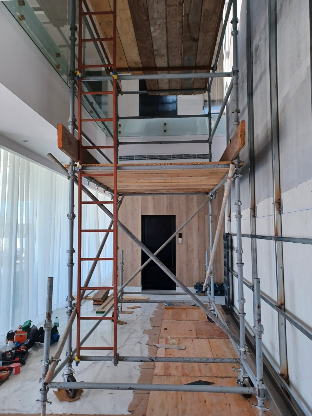 Front view of a tall mobile access scaffold with cross bracing and two timber work platforms indoors