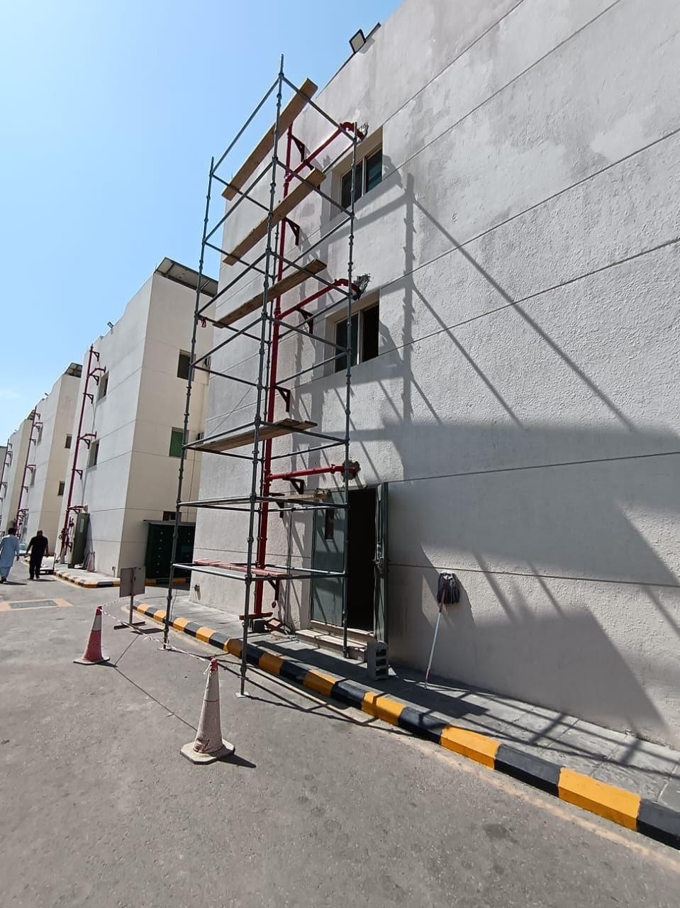 Scaffolding structure alongside a facility exterior supporting red fire suppression pipework with site safety cones