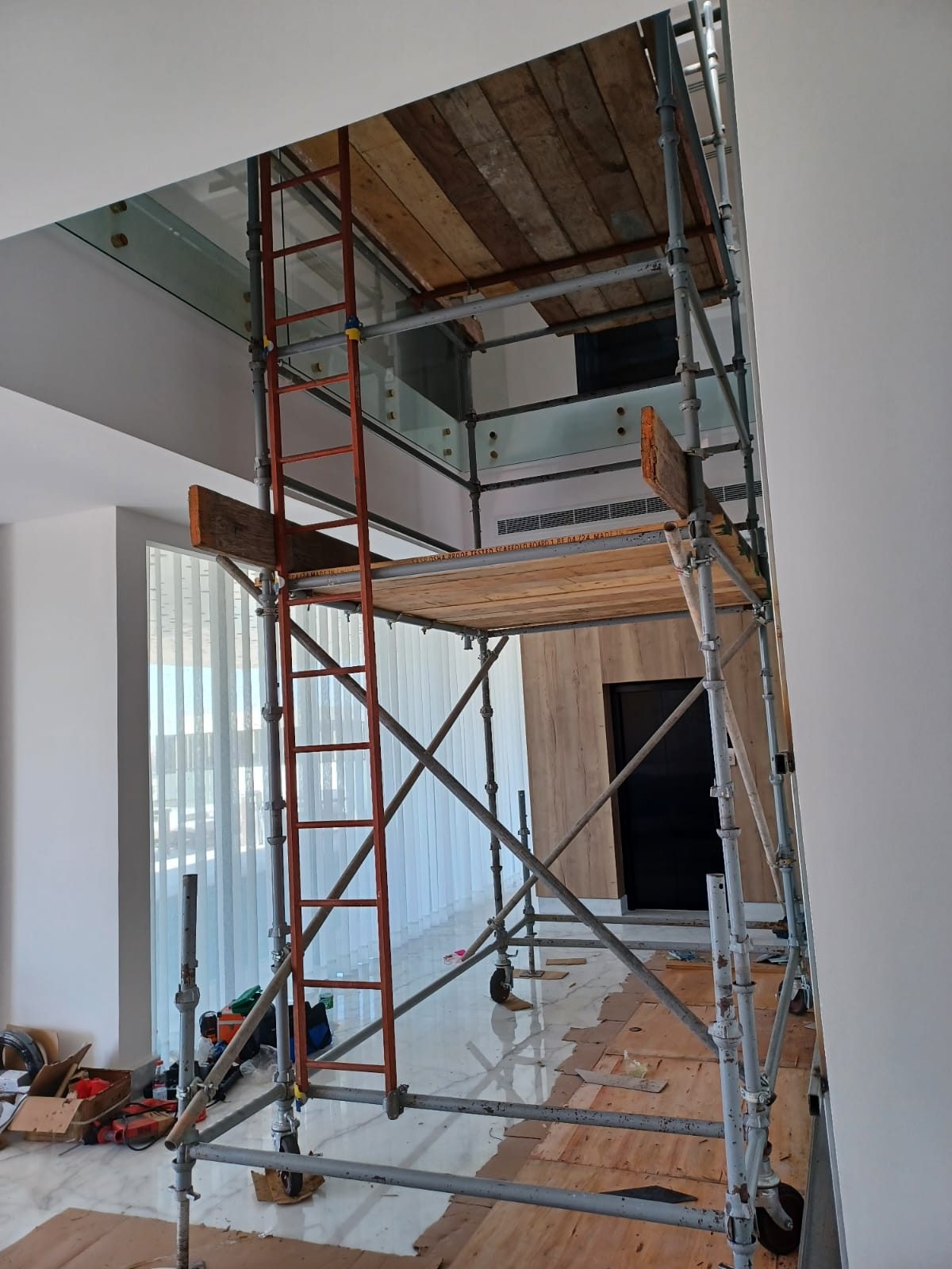 Full-height interior scaffold tower erected along a wall with rolling base, cross bracing and ladder access