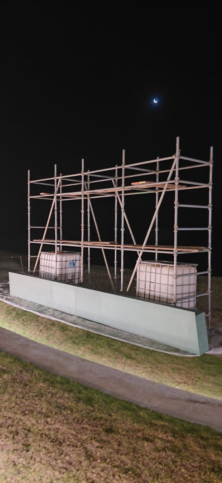 Scaffold access tower with timber decking alongside a palm-lined resort walkway at night