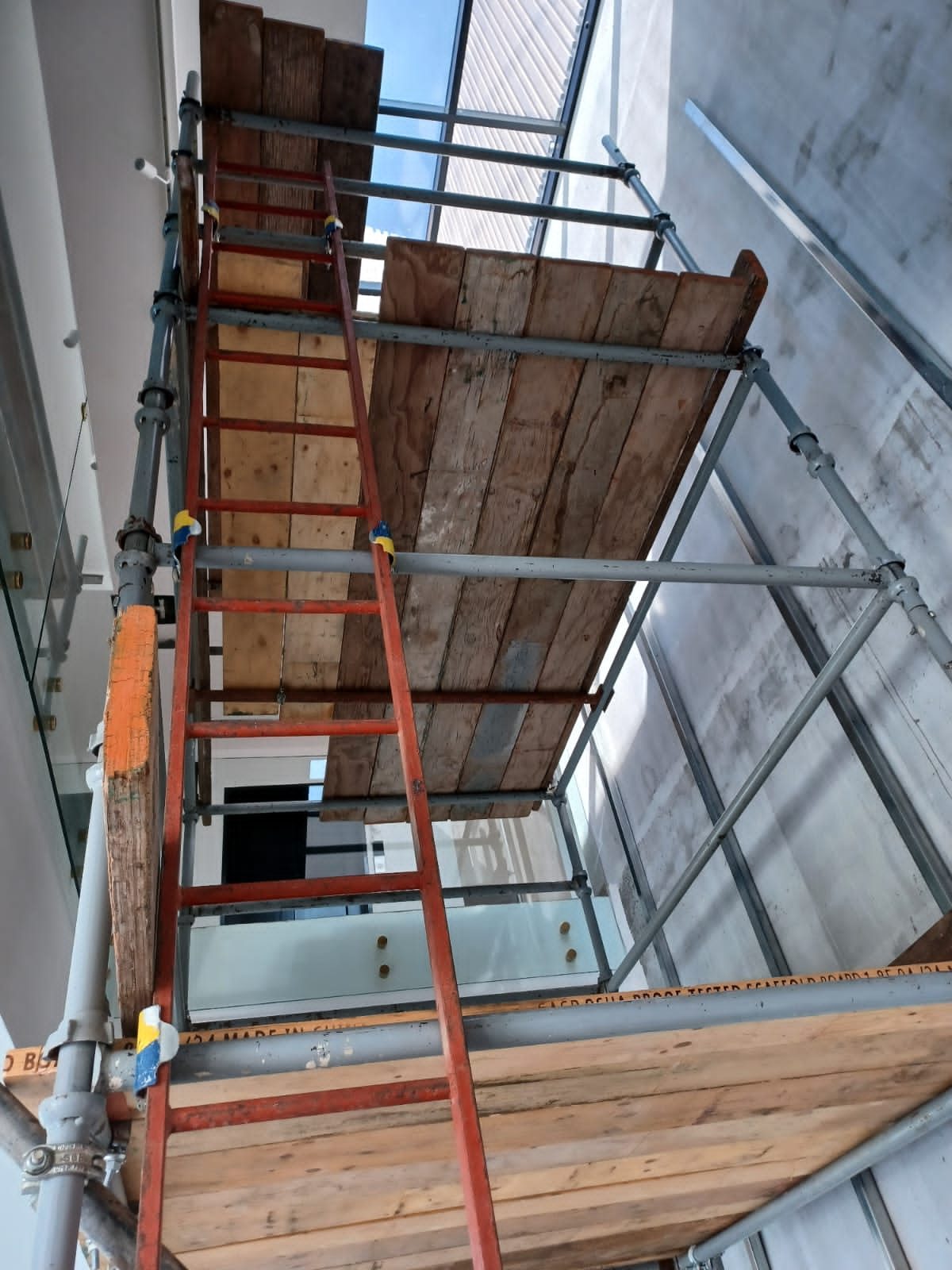 Close upward view of a scaffold ladder and timber platform beneath a double-height skylight
