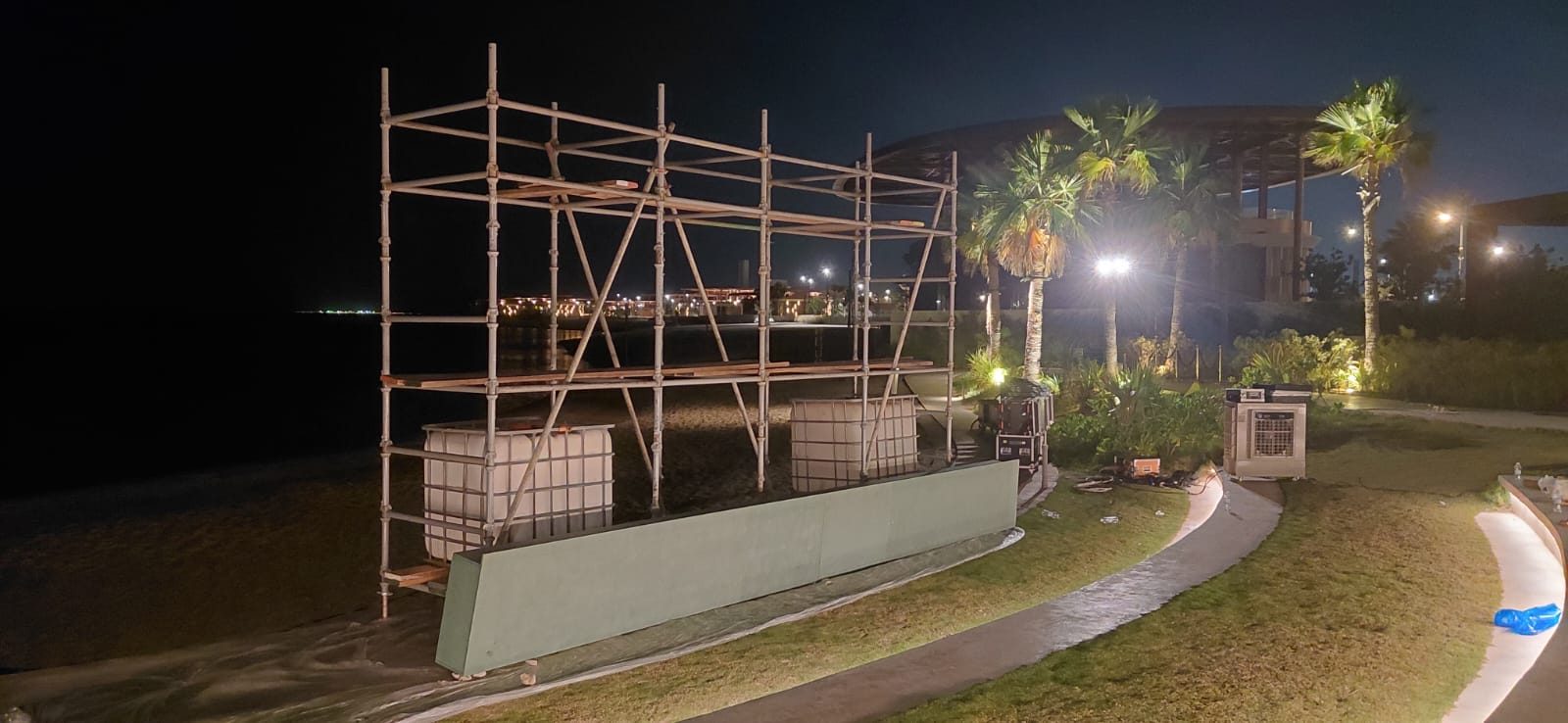 Tube-and-clamp scaffolding with timber platforms installed on a landscaped resort sand area at night