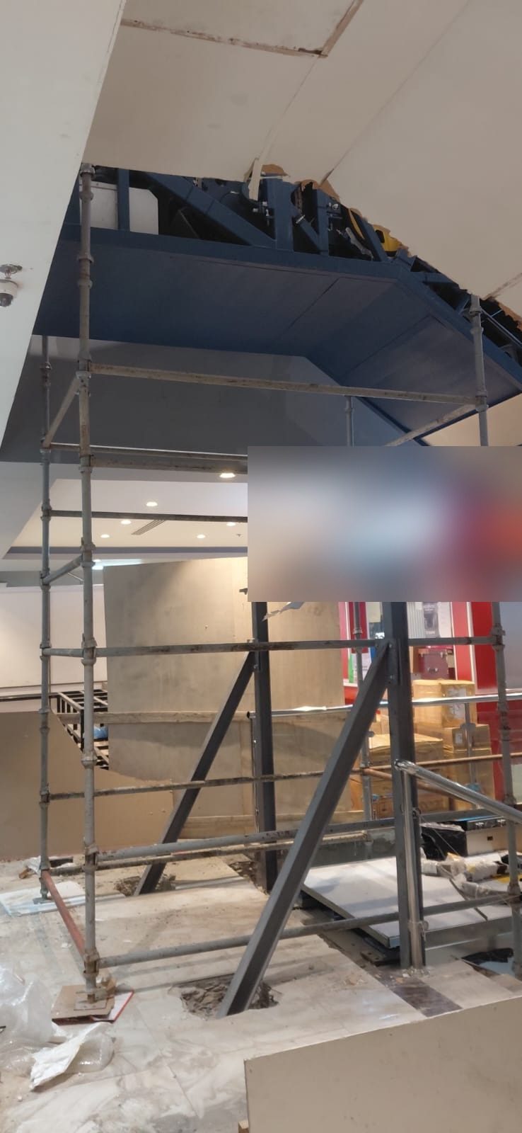 Structural-level scaffolding surrounding an escalator opening inside a commercial building